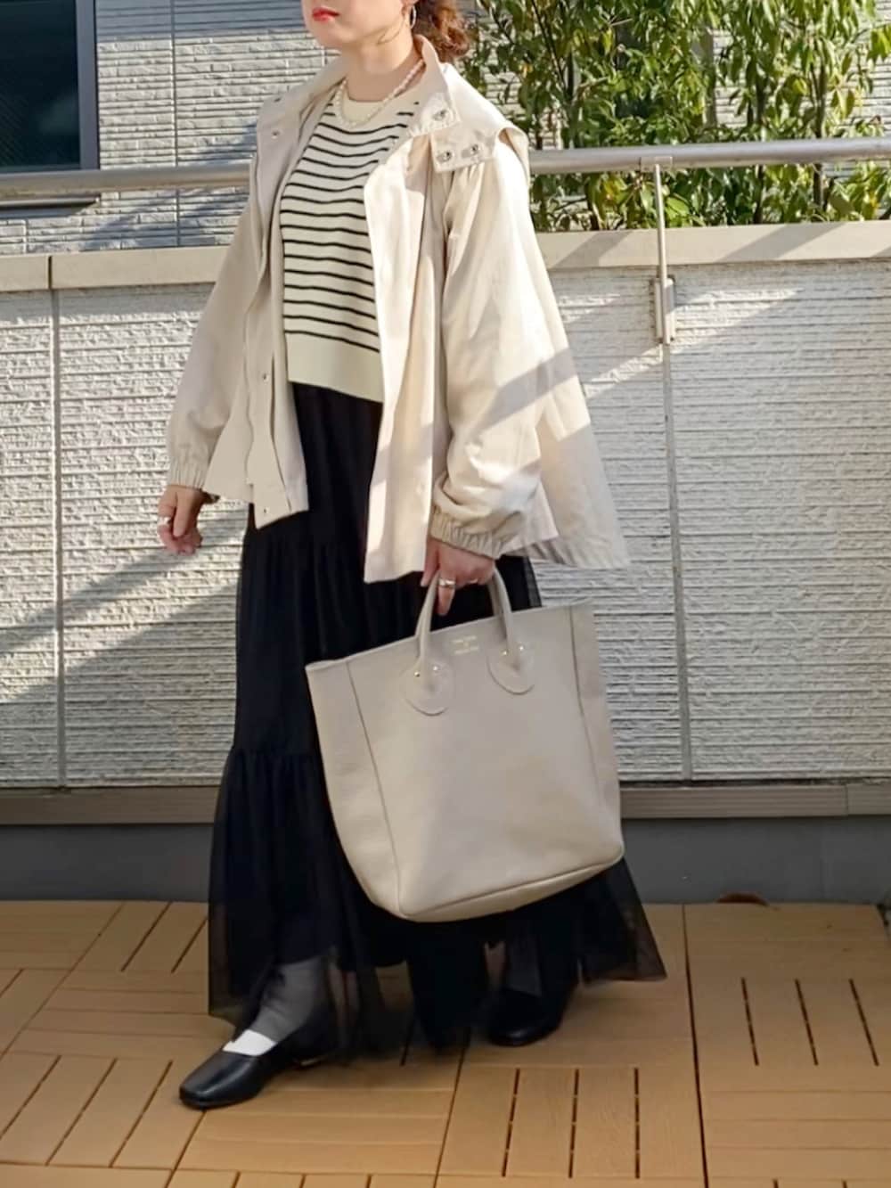 ホワイト系のマウンテンパーカー、ブラック系のカーディガン/ボレロ、ブラック系のスカートを着用したレディースの春コーディネートの2枚目の写真