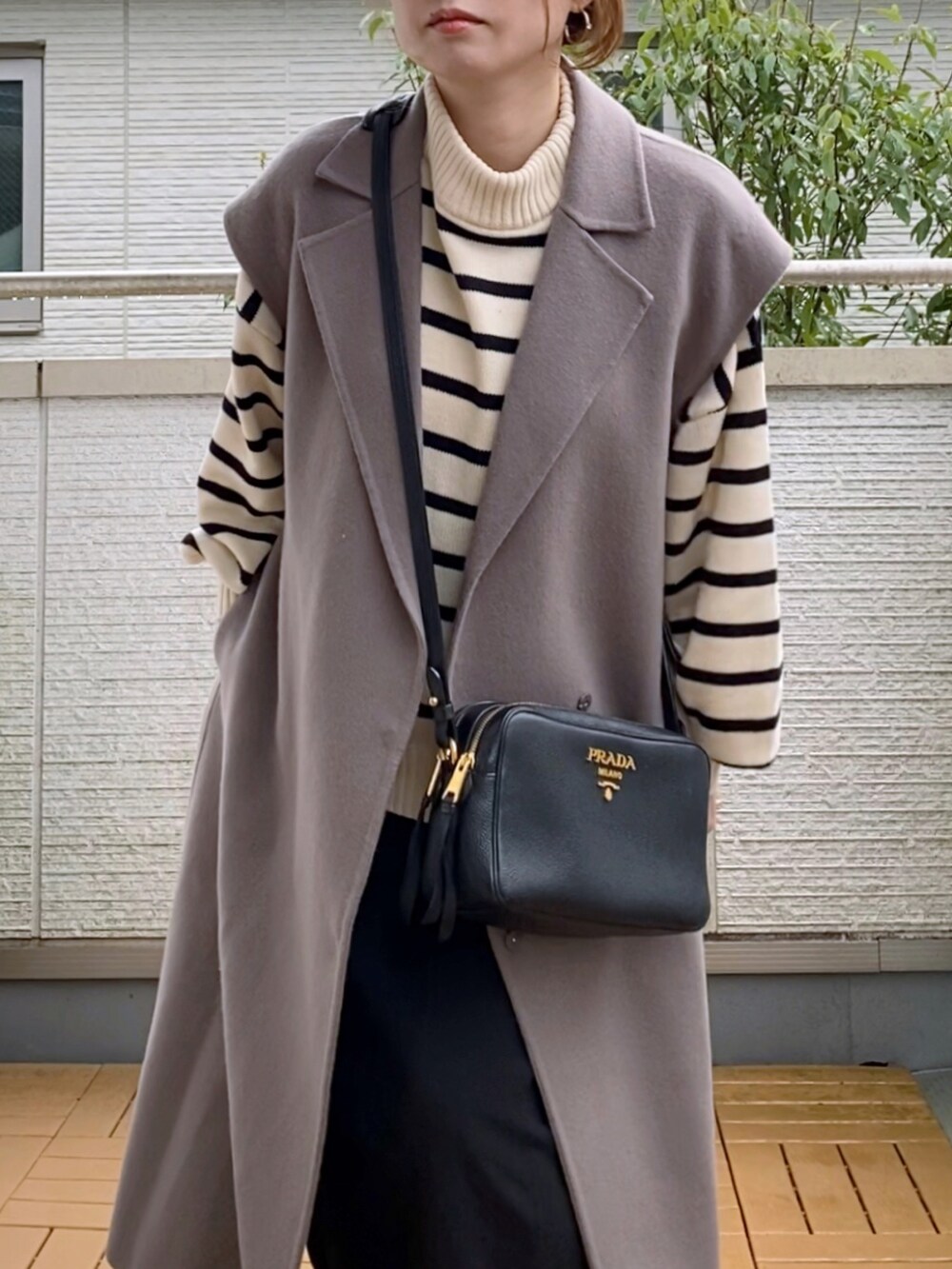 ブラウン系のチェスターコート、ホワイト系のニット/セーター、ブラック系のスカートを着用したレディースの秋コーディネートの3枚目の写真