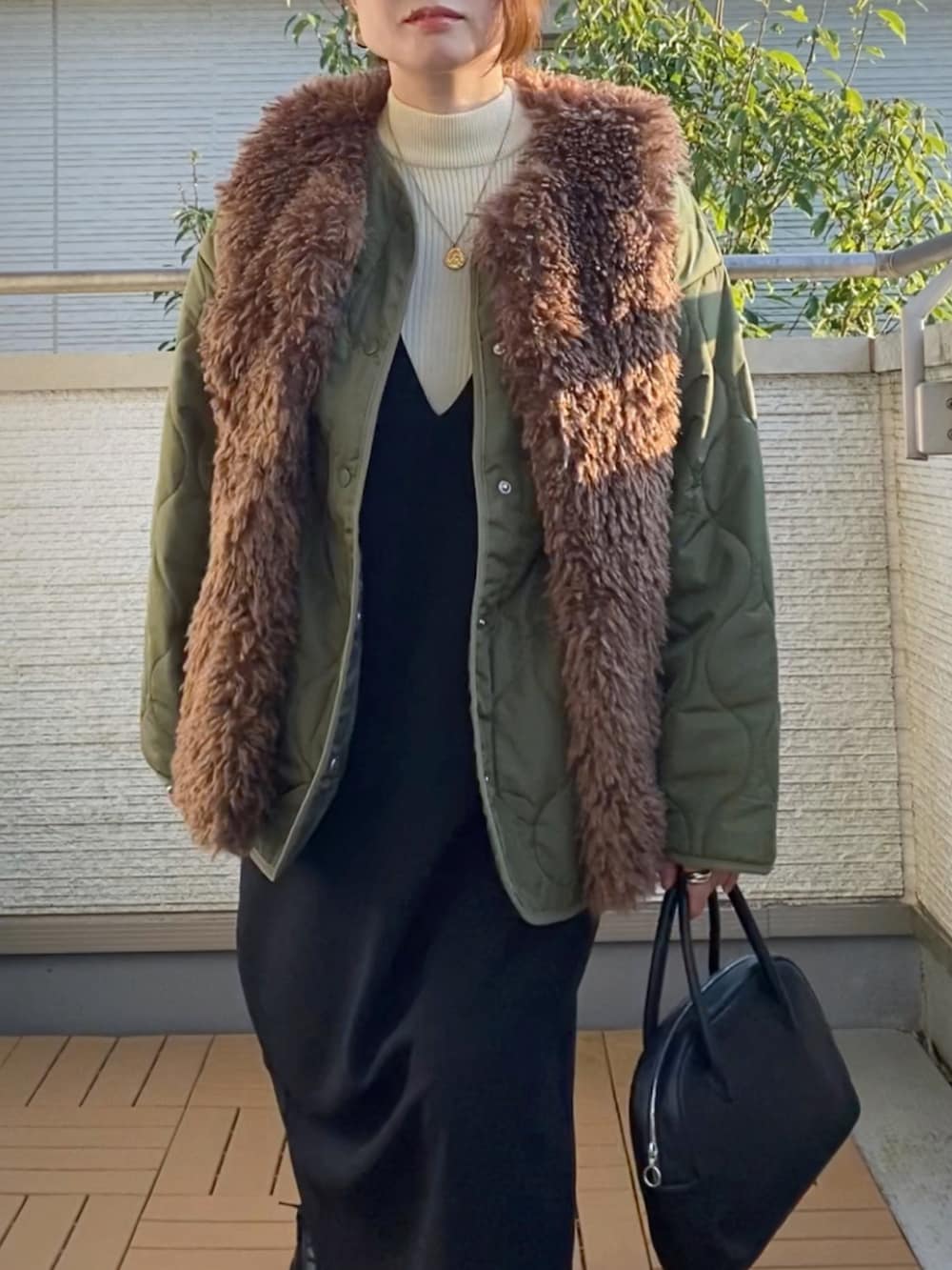 グリーン系のブルゾン、ブラック系のジャンパースカート、ホワイト系のニット/セーターを着用したレディースの秋コーディネートの2枚目の写真