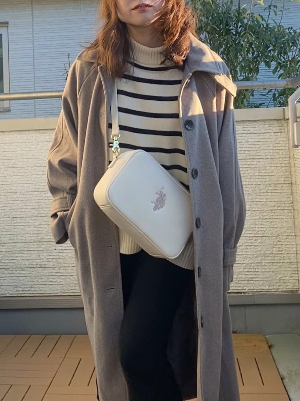 ブラウン系のステンカラーコート、ホワイト系のニット/セーター、ホワイト系のショルダーバッグを着用したレディースの冬コーディネートの2枚目の写真