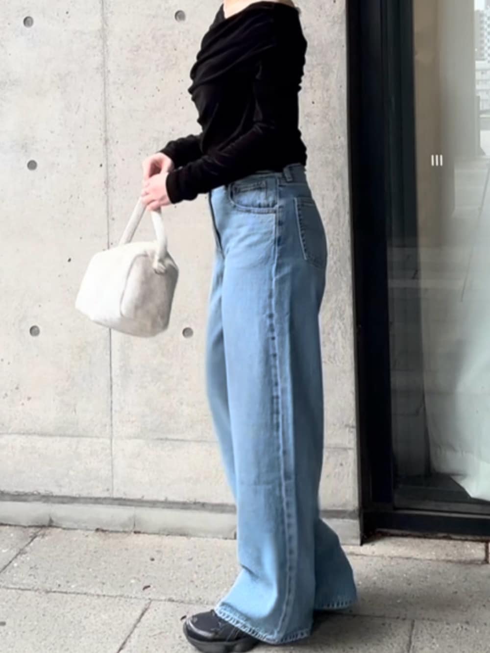 ブルー系のデニムパンツ、ホワイト系のハンドバッグ、ブラック系のTシャツ/カットソーを着用したレディースの秋コーディネートの2枚目の写真