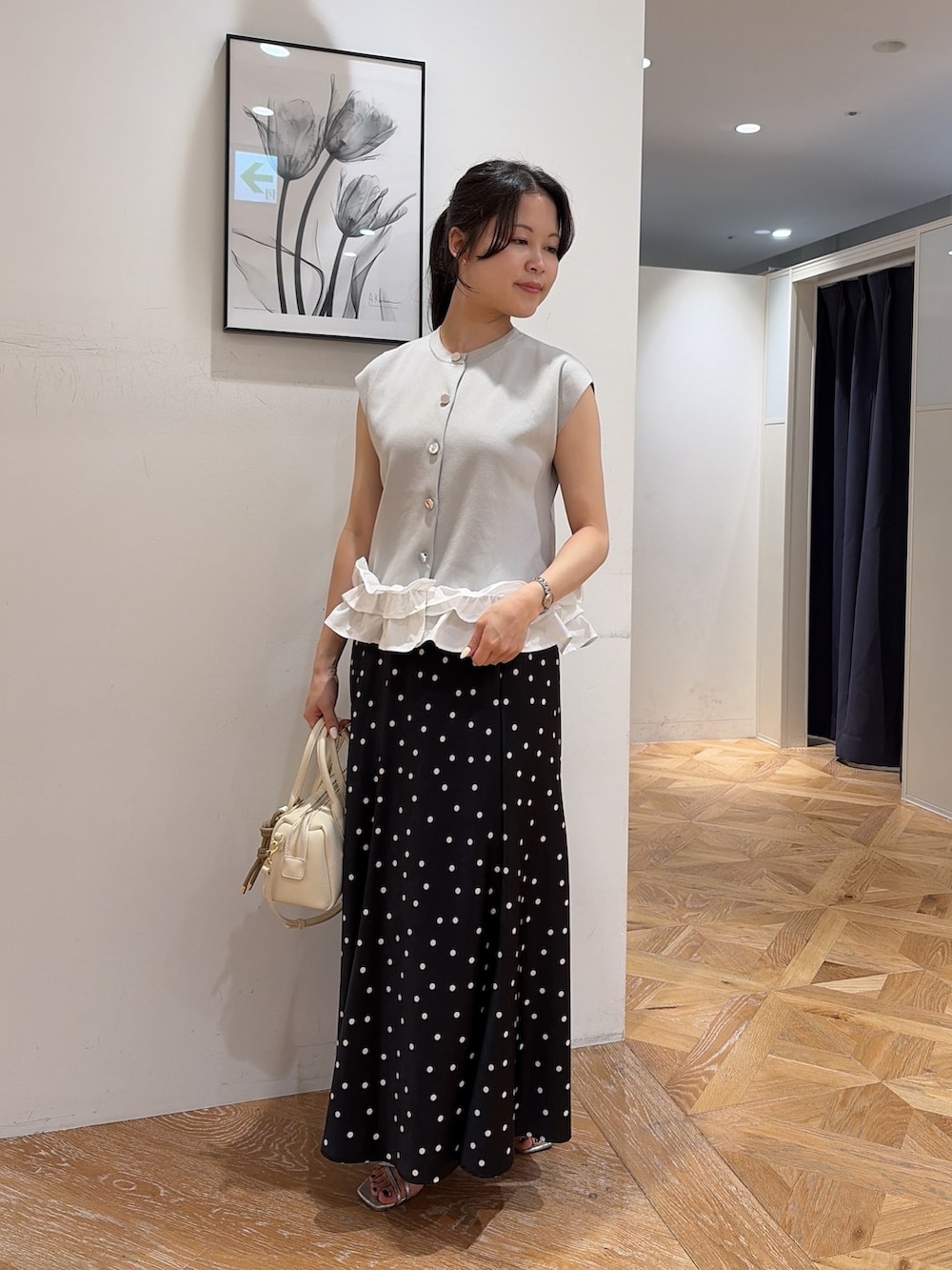グレー系のベスト、ブラック系のスカート、ホワイト系のボストンバッグを着用したレディースの夏コーディネートの2枚目の写真