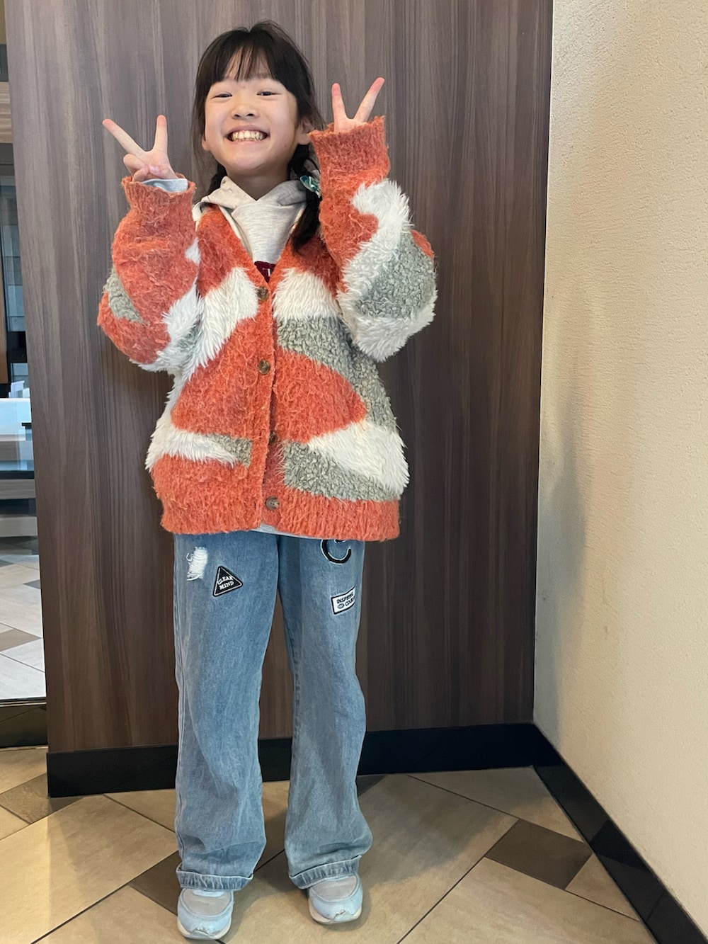 ホワイト系のパーカー、オレンジ系のカーディガン/ボレロ、ブルー系のデニムパンツを着用したキッズの冬コーディネートの2枚目の写真