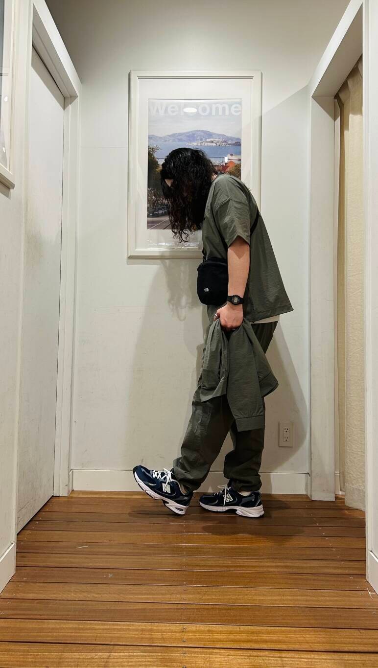 ブルー系のスニーカー、ブラック系のショルダーバッグ、グリーン系のブルゾンを着用したメンズの春コーディネートの2枚目の写真