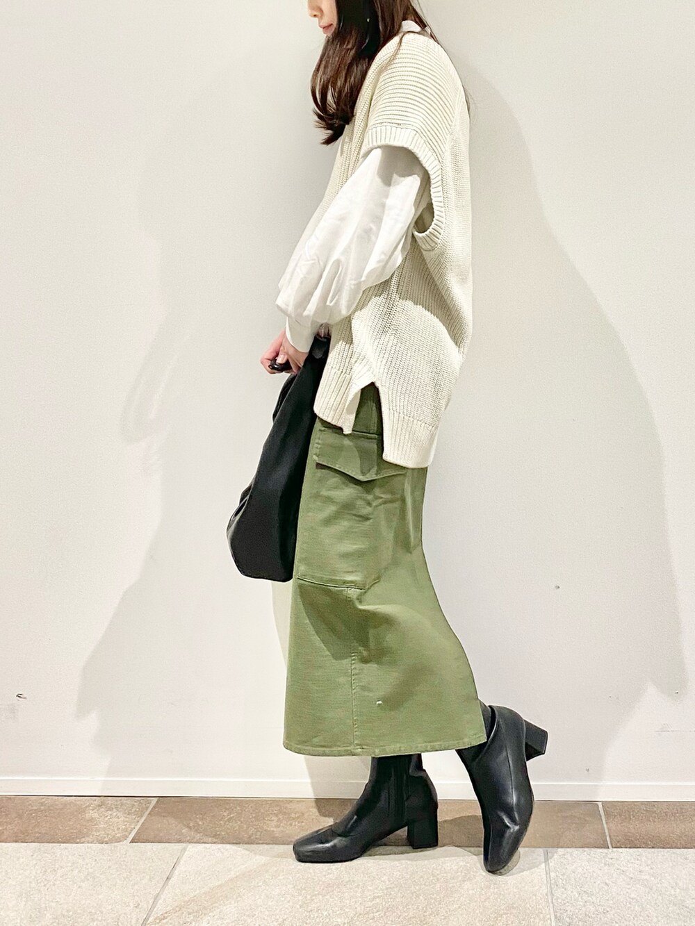ホワイト系のハンドバッグ、ホワイト系のベスト、グリーン系のスカートを着用したレディースの冬コーディネートの2枚目の写真