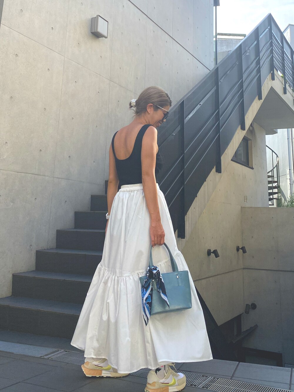 ブラック系のタンクトップ、ホワイト系のスカート、ブルー系のトートバッグを着用したレディースの夏コーディネートの2枚目の写真