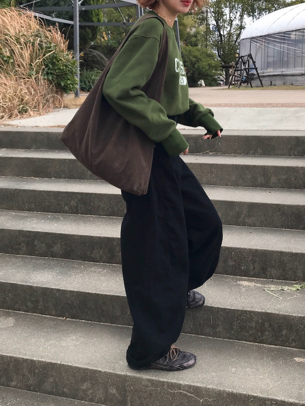 グリーン系のスウェット、ブラック系のデニムパンツ、ブラウン系のバッグを着用したレディースの冬コーディネートの3枚目の写真