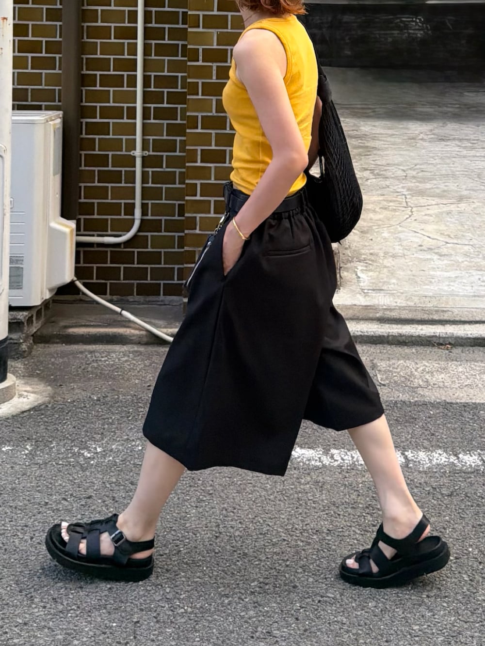 イエロー系のタンクトップ、ブラック系のパンツ、ブラック系のサンダルを着用したレディースの夏コーディネートの2枚目の写真