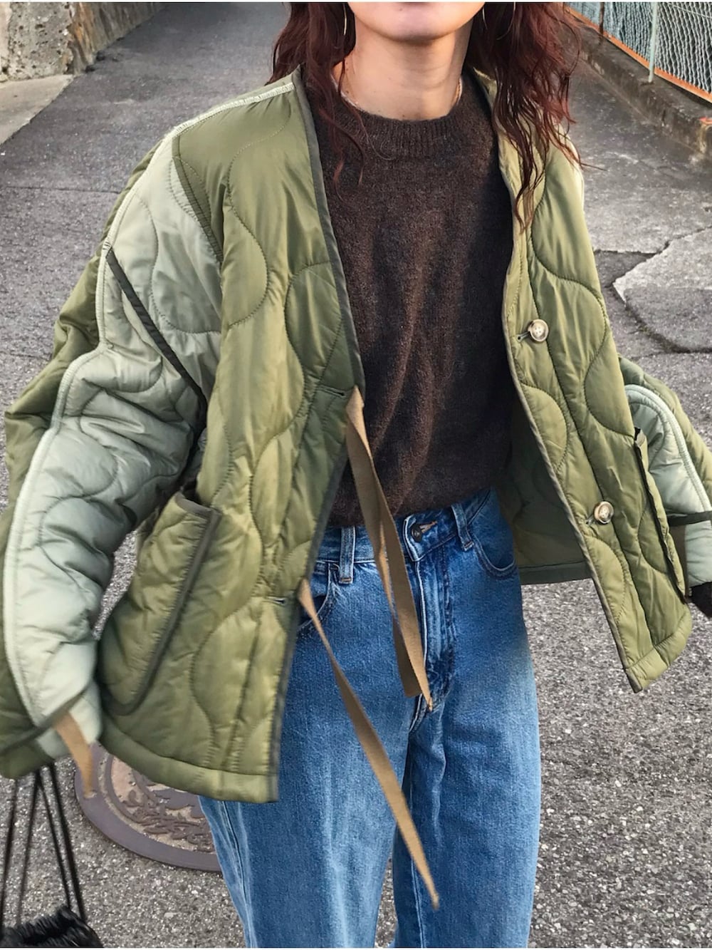 グリーン系のジャケット/アウター、ブラウン系のニット/セーター、ブルー系のデニムパンツを着用したレディースの冬コーディネートの2枚目の写真