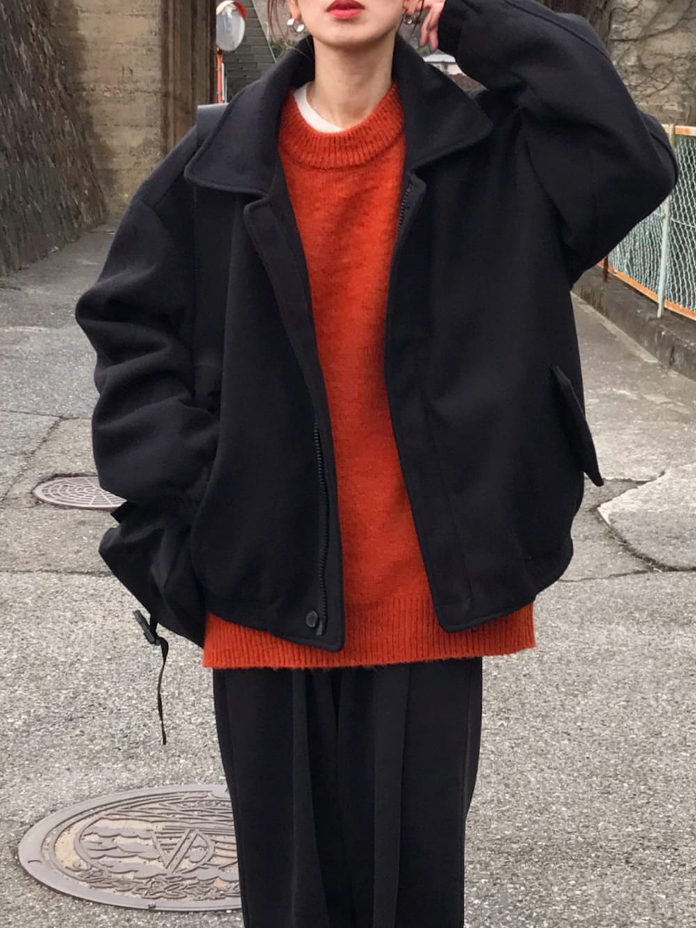 ブラック系のジャケット/アウター、オレンジ系のニット/セーター、ブラック系のショルダーバッグを着用したレディースの冬コーディネートの2枚目の写真