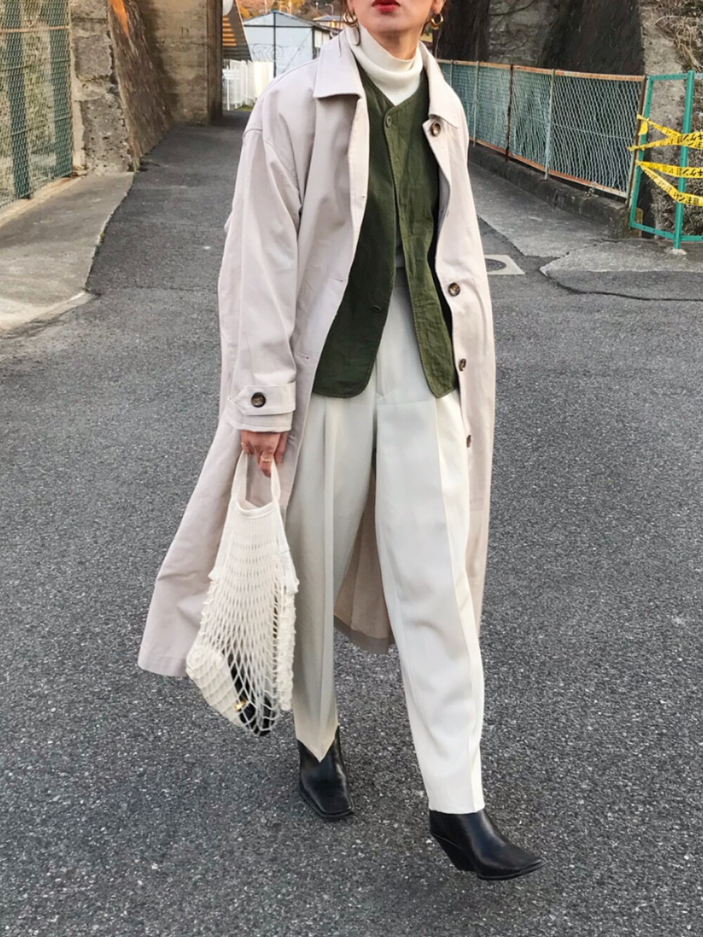 ホワイト系のステンカラーコート、グリーン系のベスト、ホワイト系のTシャツ/カットソーを着用したレディースの冬コーディネートの2枚目の写真
