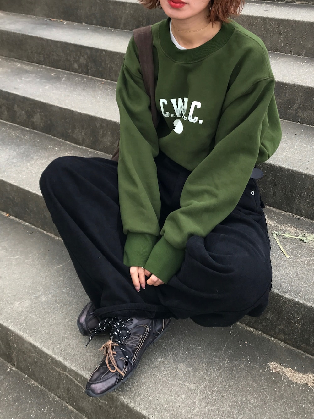 グリーン系のスウェット、ブラック系のデニムパンツ、ブラウン系のバッグを着用したレディースの冬コーディネートの2枚目の写真