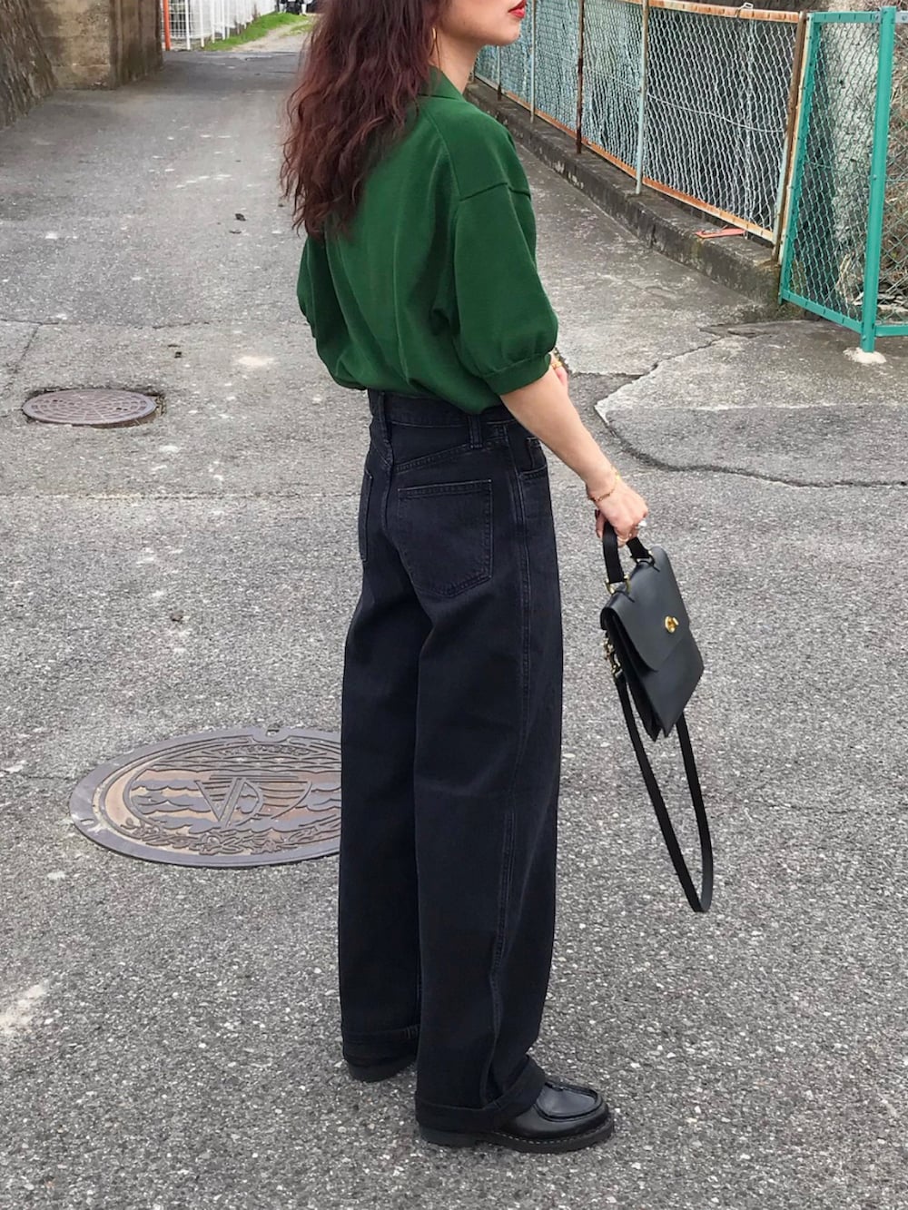グリーン系のトップス、ブラック系のデニムパンツ、ブラック系のショルダーバッグを着用したレディースの夏コーディネートの2枚目の写真