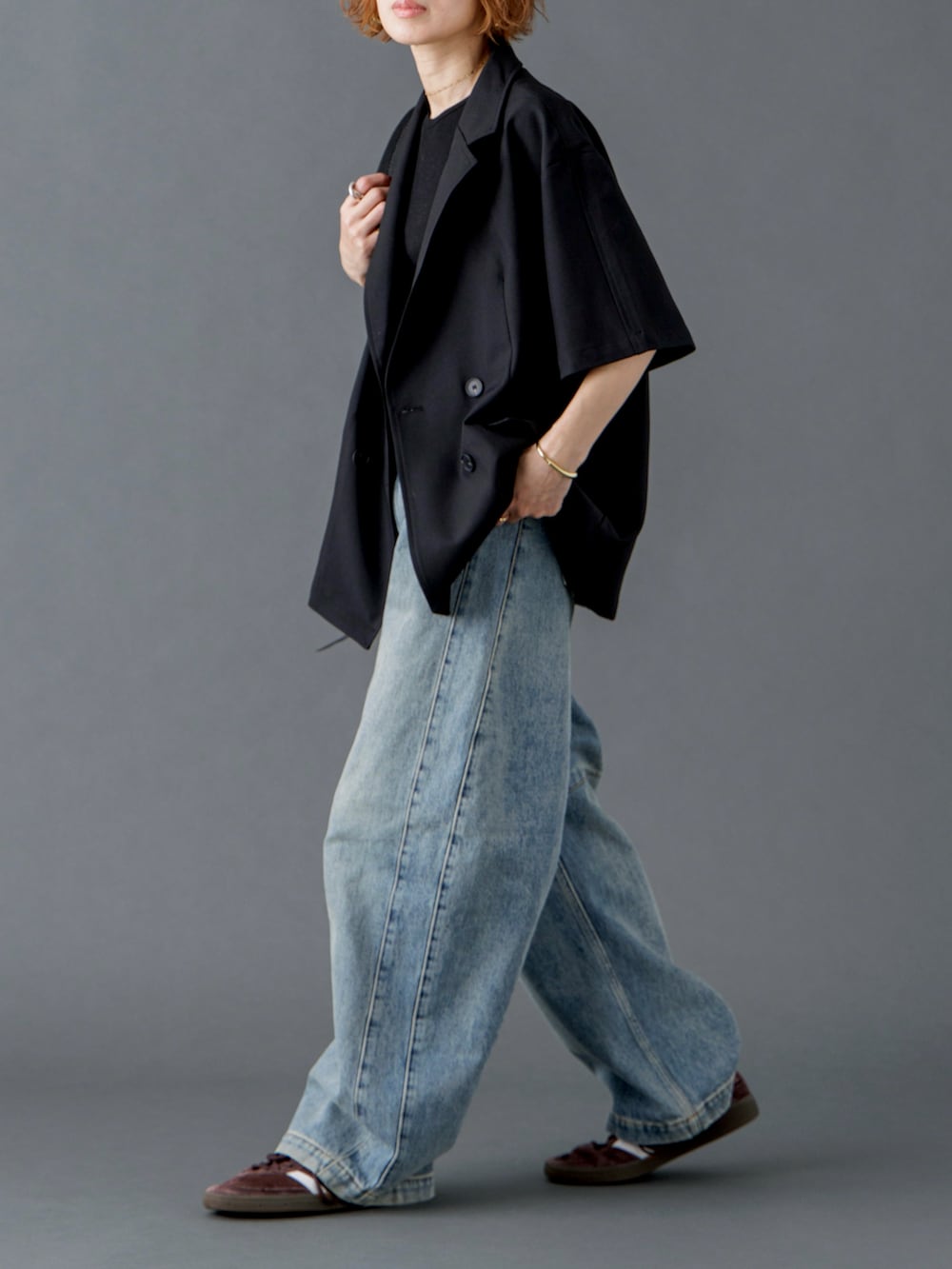 ブラック系のテーラードジャケット、ブルー系のデニムパンツ、ブラウン系のスニーカーを着用したレディースの春コーディネートの2枚目の写真