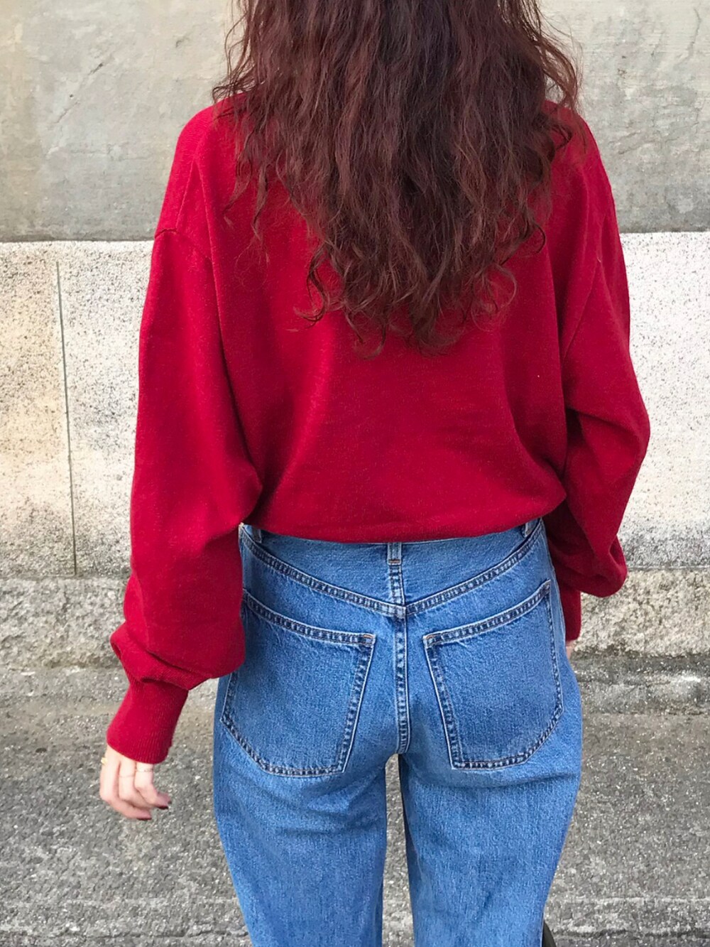 レッド系のニット/セーター、ブルー系のデニムパンツ、グリーン系のバッグを着用したレディースの秋コーディネートの2枚目の写真