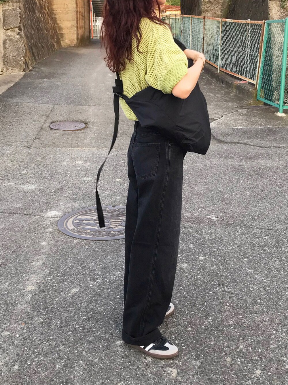 グリーン系のトップス、ブラック系のデニムパンツ、ブラック系のショルダーバッグを着用したレディースの夏コーディネートの2枚目の写真