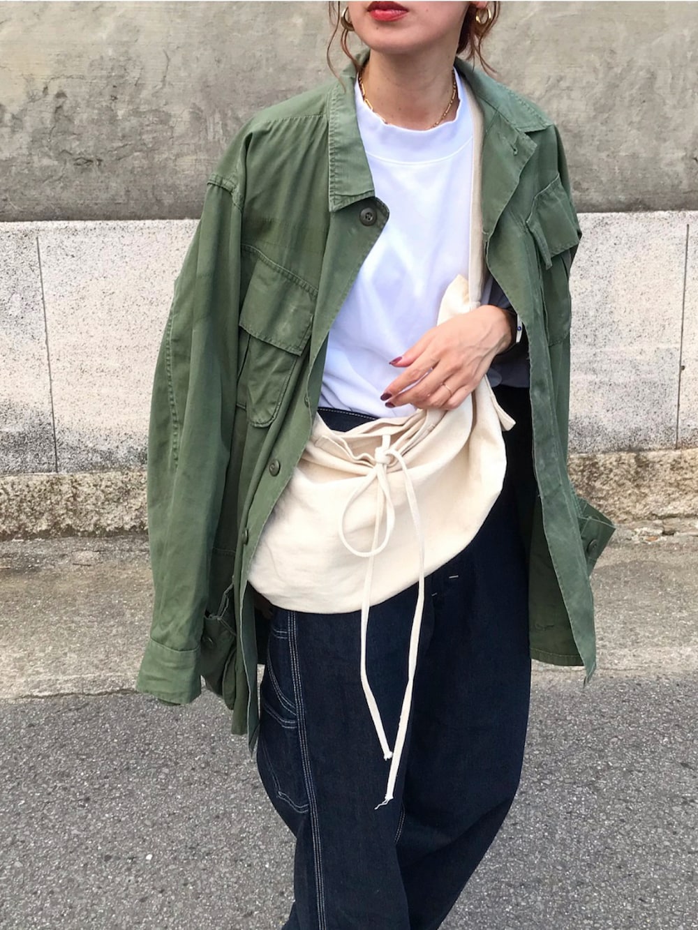 グリーン系のミリタリージャケット、ホワイト系のTシャツ/カットソー、ブルー系のデニムパンツを着用したレディースの夏コーディネートの2枚目の写真
