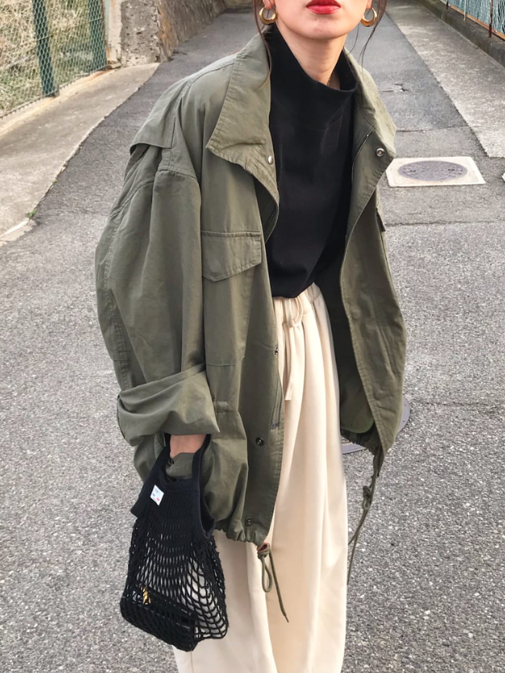 グリーン系のミリタリージャケット、ブラック系のトップス、ホワイト系のスウェットパンツを着用したレディースの春コーディネートの2枚目の写真