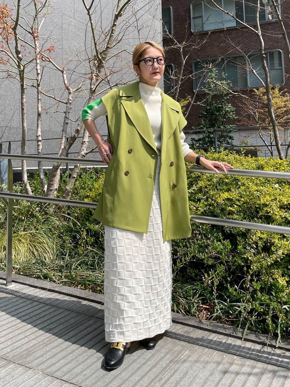 グリーン系のベスト、ホワイト系のニット/セーター、ホワイト系のスカートを着用したレディースの春コーディネートの2枚目の写真