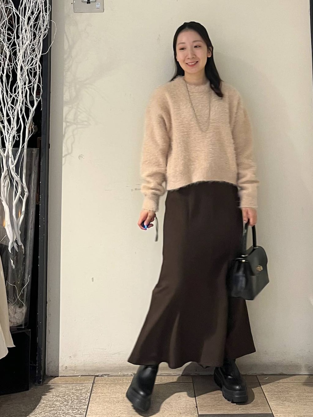 ブラック系のボストンバッグ、ブラウン系のスカート、ブラック系のブーツを着用したレディースの冬コーディネートの2枚目の写真
