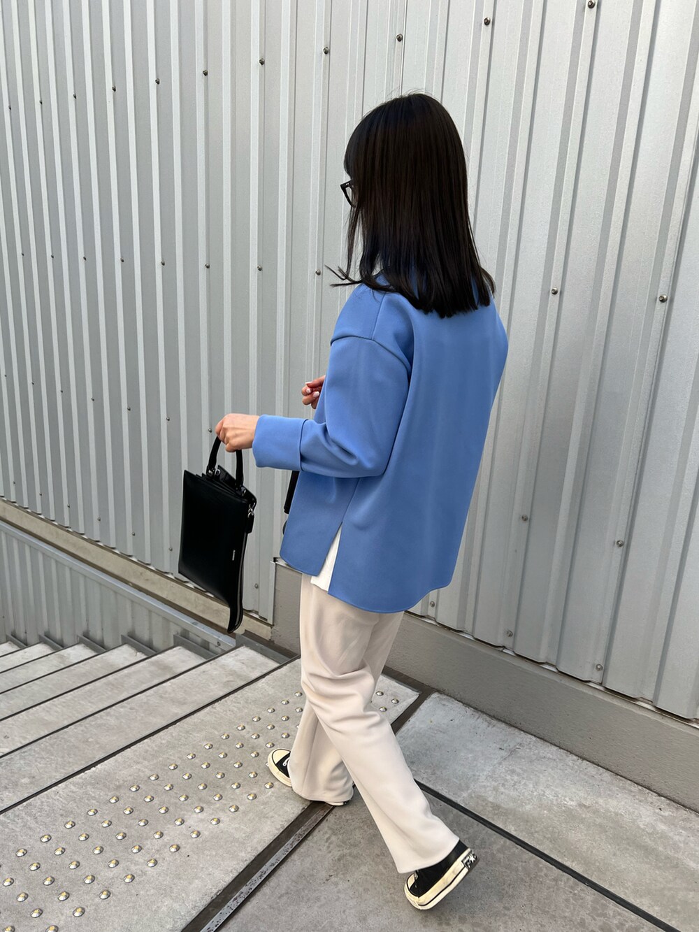 ブラック系のライダースジャケット、ホワイト系のスラックス、ブラック系のスニーカーを着用したレディースの春コーディネートの2枚目の写真