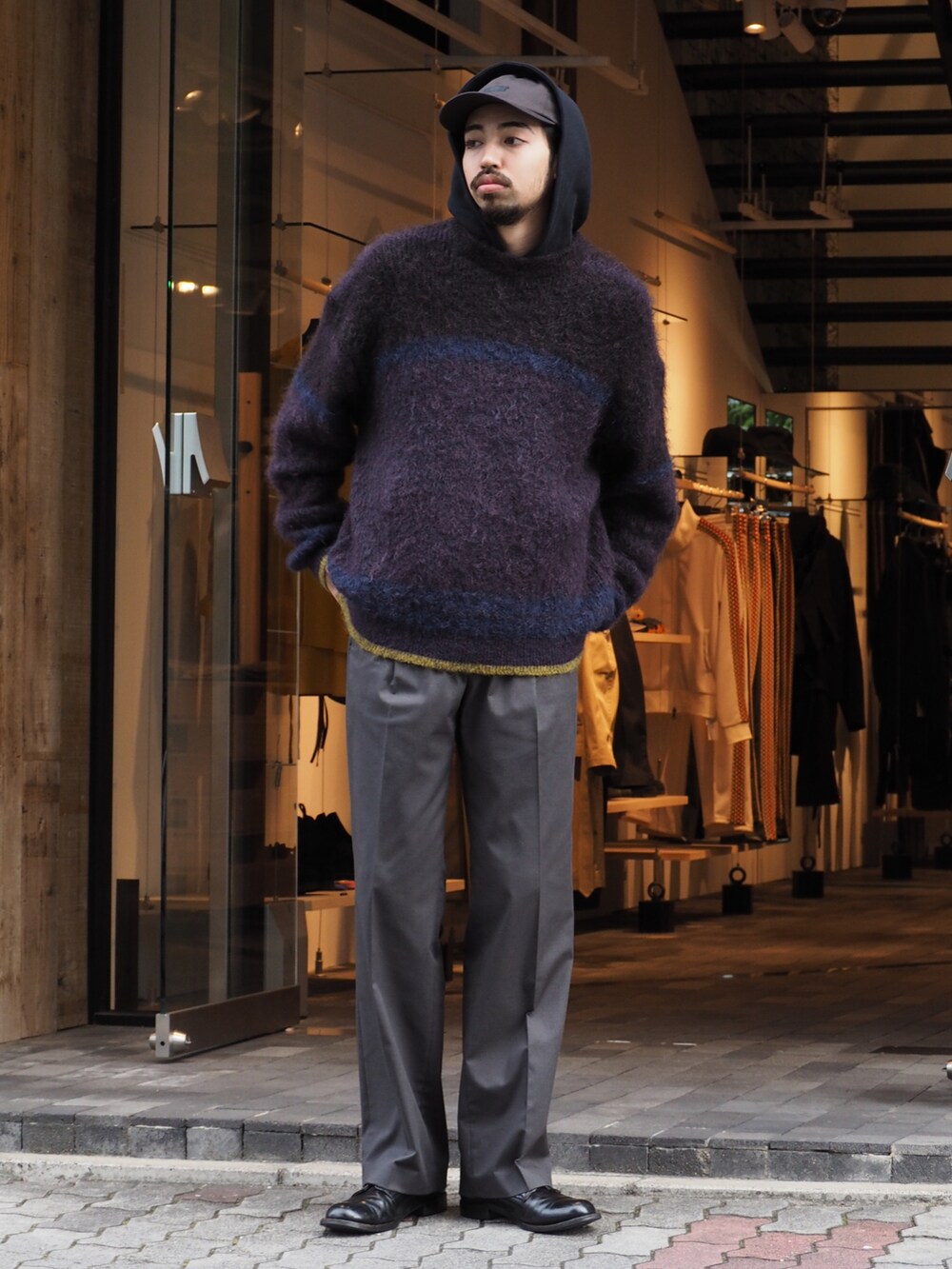 パープル系のニット/セーター、グレー系のスラックス、ブラック系のパーカーを着用したメンズの秋コーディネートの2枚目の写真