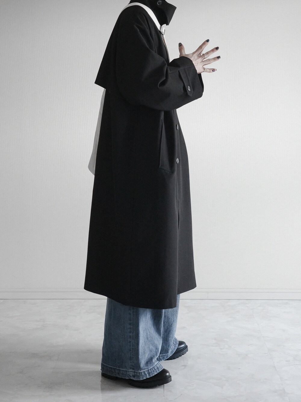 ブラック系のステンカラーコート、ブルー系のデニムパンツ、ブラック系のブーツを着用したメンズの冬コーディネートの2枚目の写真