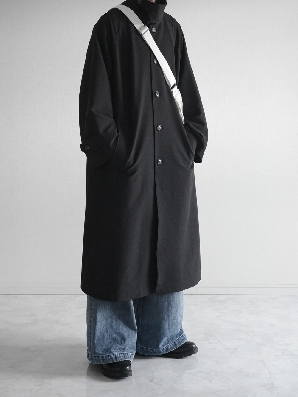 ブラック系のステンカラーコート、ブルー系のデニムパンツ、ブラック系のブーツを着用したメンズの冬コーディネートの3枚目の写真