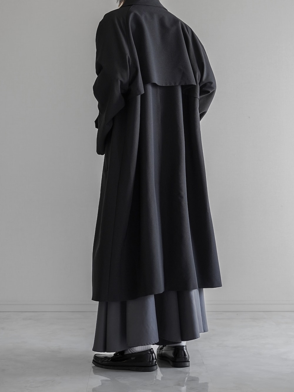 ブラック系のステンカラーコート、ホワイト系のTシャツ/カットソー、グレー系のスラックスを着用したメンズの秋コーディネートの4枚目の写真