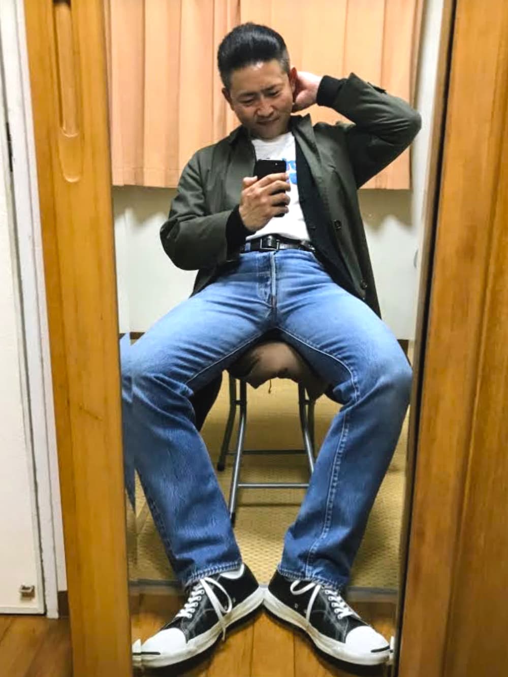 グリーン系のステンカラーコート、ブラック系のカーディガン/ボレロ、ホワイト系のTシャツ/カットソーを着用したメンズの冬コーディネートの2枚目の写真