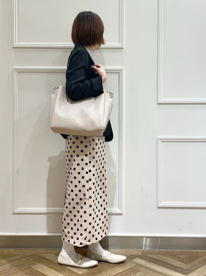 ブラック系のノーカラージャケット、グレー系のニット/セーター、ベージュ系のスカートを着用したレディースの春コーディネートの2枚目の写真