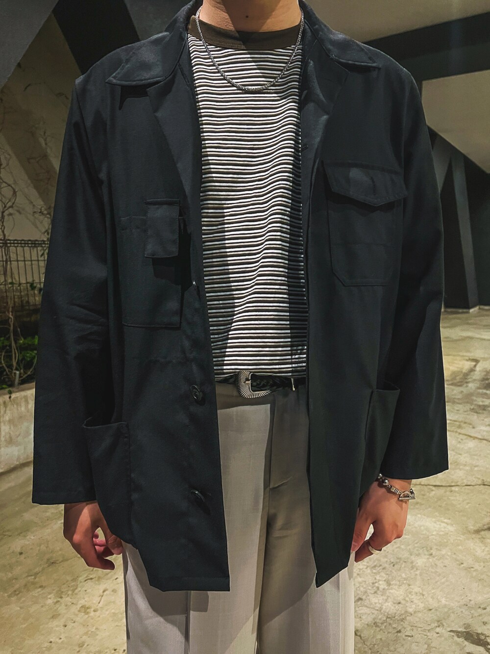 ブラック系のブルゾン、ブラウン系のTシャツ/カットソー、ベージュ系のスラックスを着用したメンズの春コーディネートの2枚目の写真