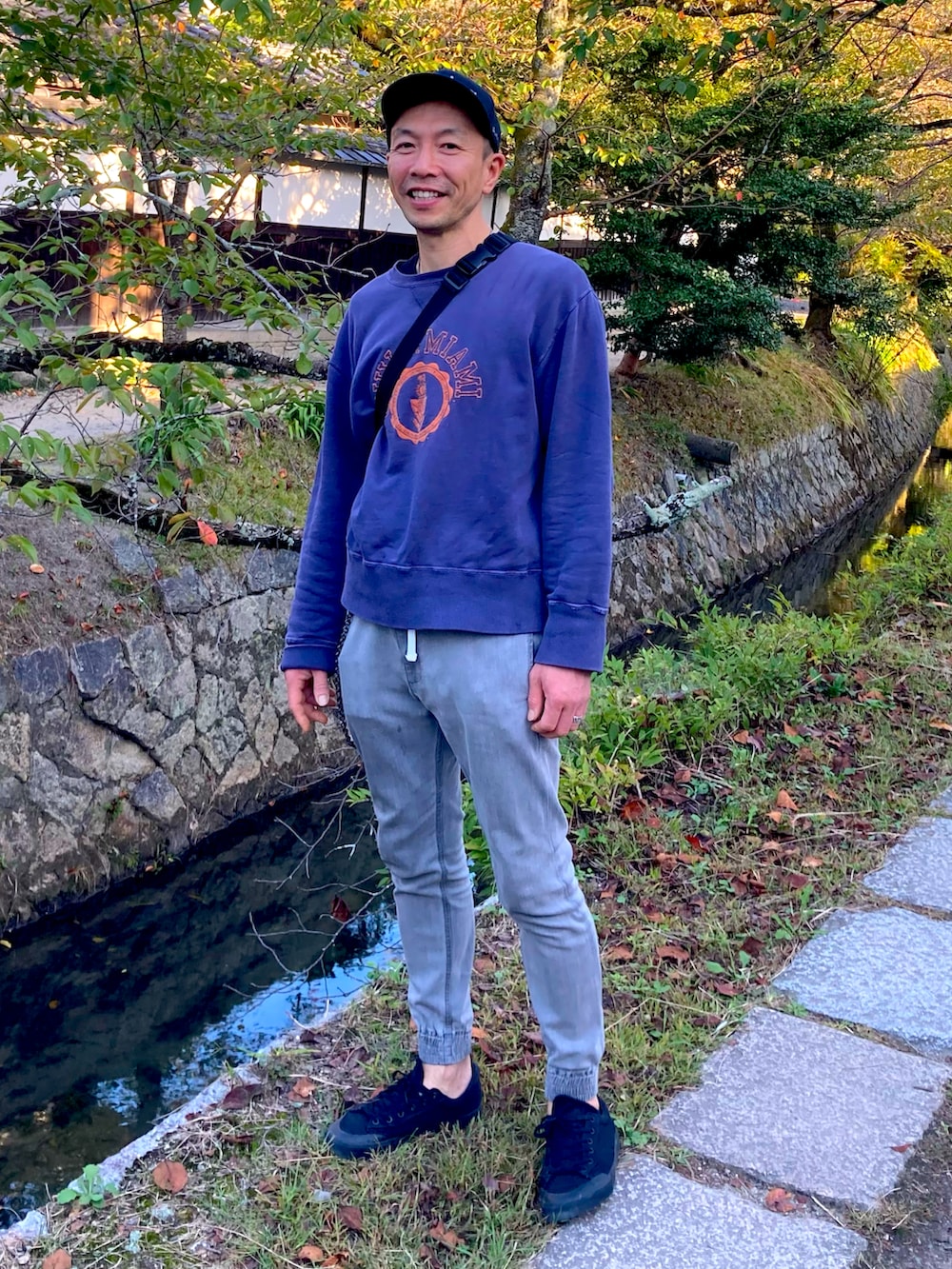 パープル系のスウェット、グリーン系のボディバッグ/ウエストポーチ、グレー系のデニムパンツを着用したメンズの秋コーディネートの2枚目の写真