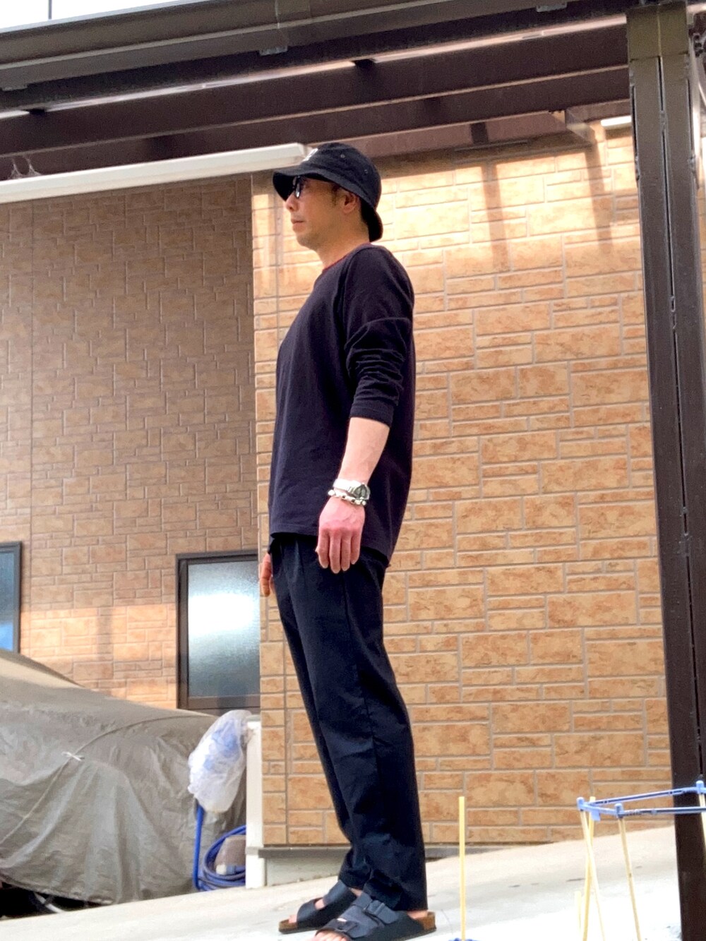 ブラック系のチノパンツ、ブラック系のTシャツ/カットソー、ブラック系のサンダルを着用したメンズの春コーディネートの2枚目の写真