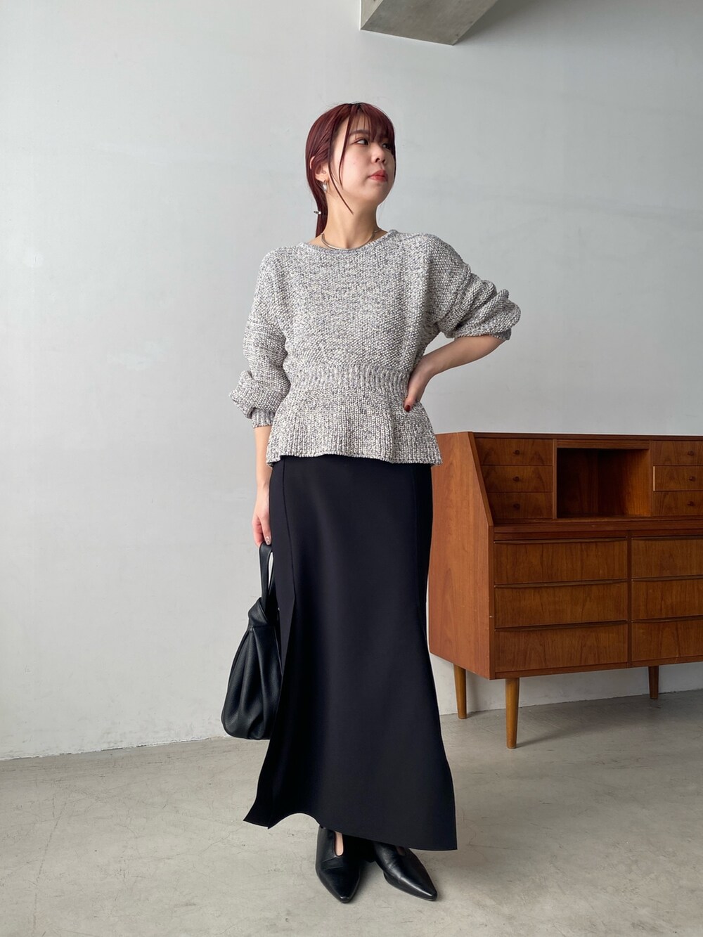 グレー系のニット/セーター、ブラック系のスカート、ブラック系のハンドバッグを着用したレディースの冬コーディネートの2枚目の写真