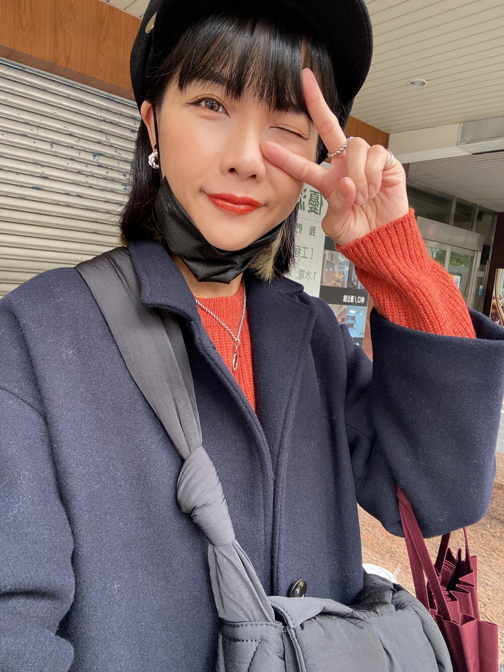 ブルー系のチェスターコート、オレンジ系のニット/セーター、ブルー系のジャンパースカートを着用したレディースの冬コーディネートの2枚目の写真