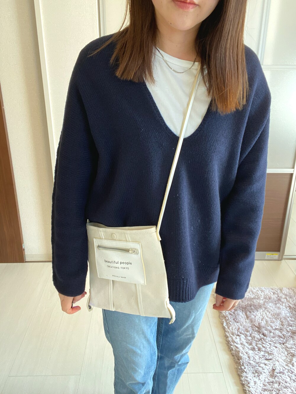 ブルー系のデニムパンツ、ホワイト系のショルダーバッグ、ブルー系のニット/セーターを着用したレディースの春コーディネートの2枚目の写真