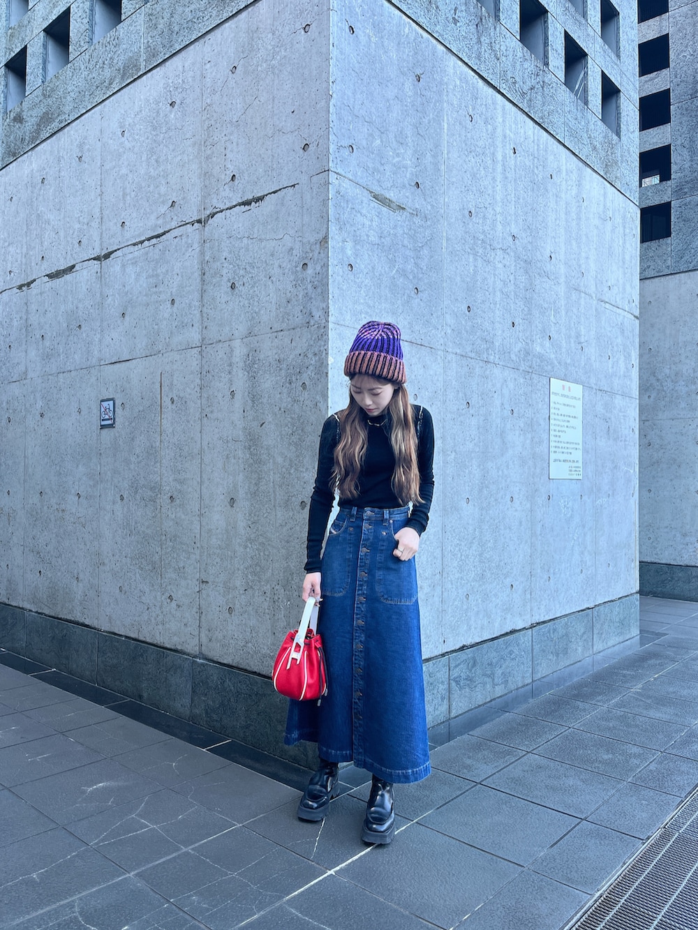 ブルー系のデニムスカート、ブラック系のニット/セーター、レッド系のハンドバッグを着用したレディースの冬コーディネートの2枚目の写真