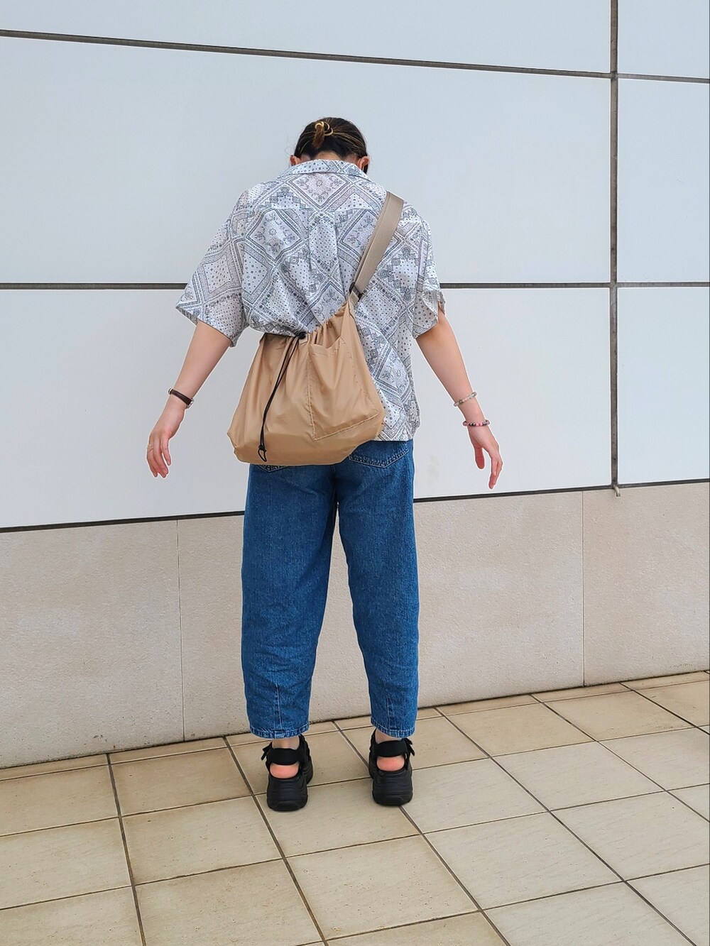 ブルー系のデニムパンツ、ブラック系のサンダル、ベージュ系のショルダーバッグを着用したレディースの夏コーディネートの2枚目の写真