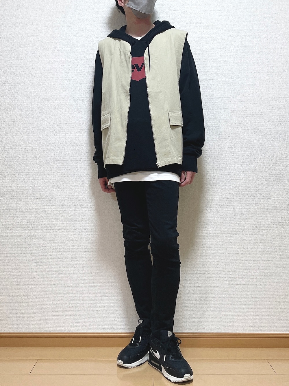 ベージュ系のベスト、ブラック系のパーカー、ブラック系のデニムパンツを着用したメンズの春コーディネートの2枚目の写真
