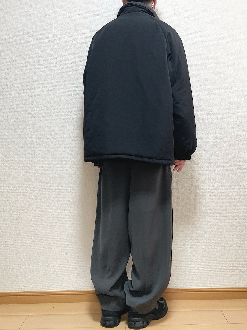 ブラック系のその他アウター、ベージュ系のニット/セーター、グレー系のスラックスを着用したメンズの春コーディネートの4枚目の写真