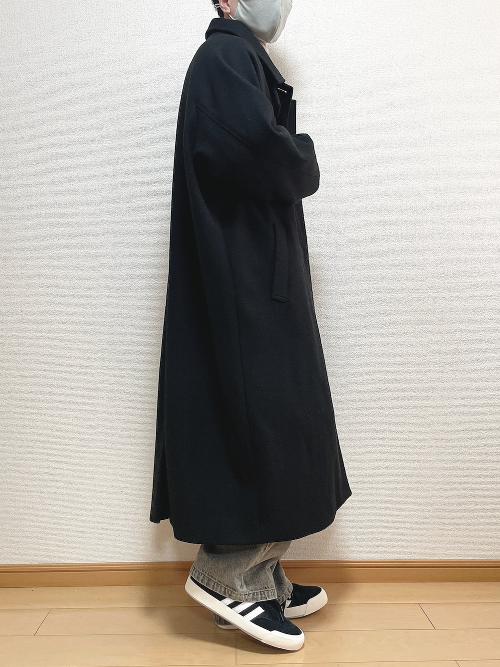 ブラック系のステンカラーコート、ベージュ系のニット/セーター、ブルー系のデニムパンツを着用したメンズの冬コーディネートの2枚目の写真