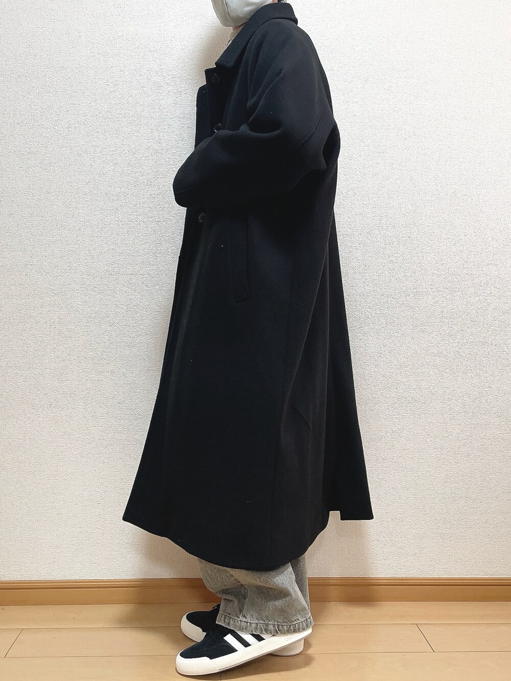 ブラック系のステンカラーコート、ベージュ系のニット/セーター、ブルー系のデニムパンツを着用したメンズの冬コーディネートの3枚目の写真