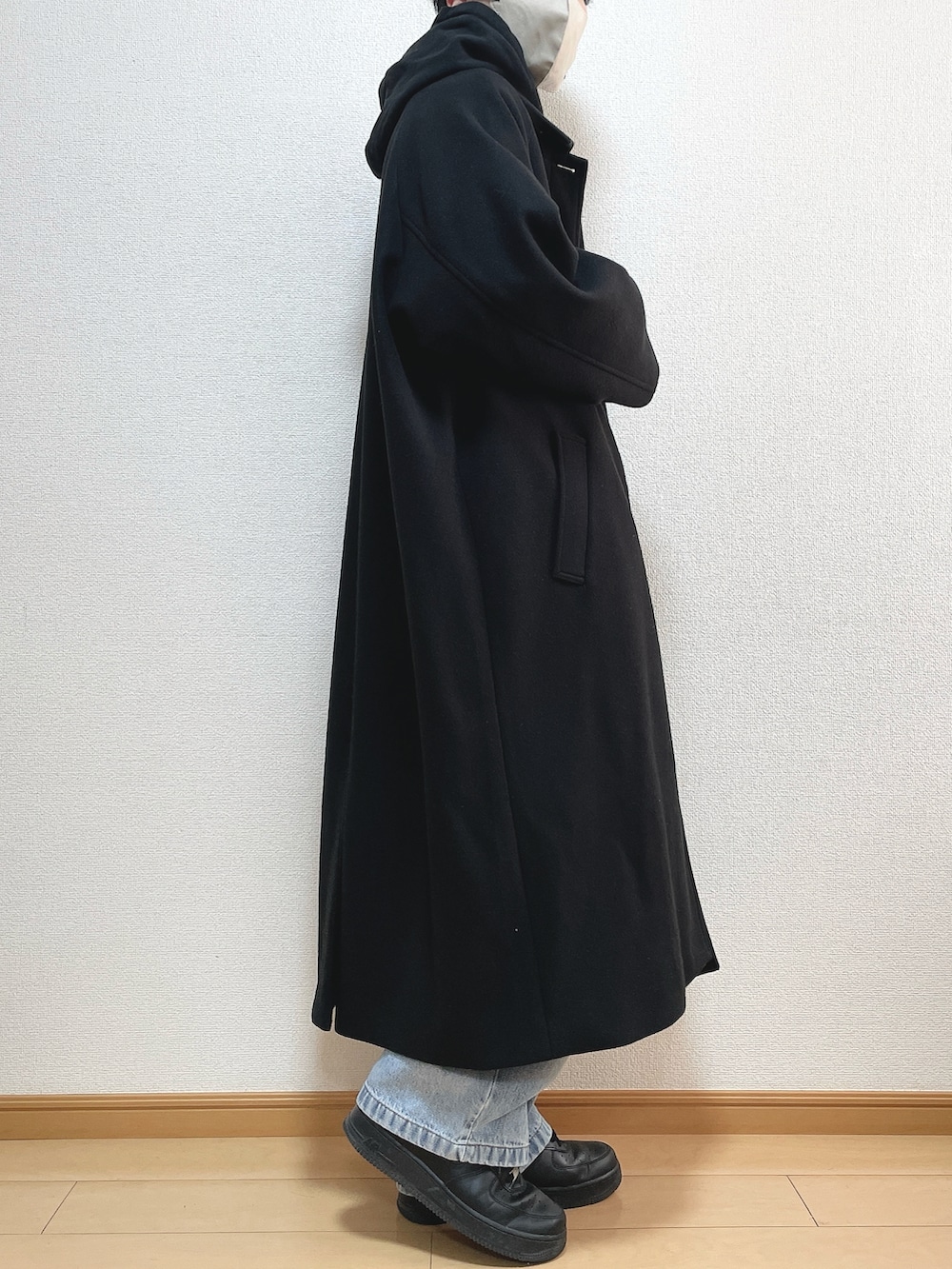 ブラック系のステンカラーコート、ブラック系のパーカー、ブルー系のデニムパンツを着用したメンズの冬コーディネートの2枚目の写真