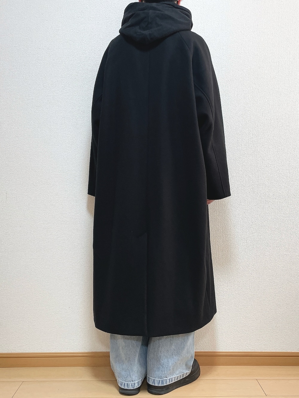 ブラック系のステンカラーコート、ブラック系のパーカー、ブルー系のデニムパンツを着用したメンズの冬コーディネートの4枚目の写真