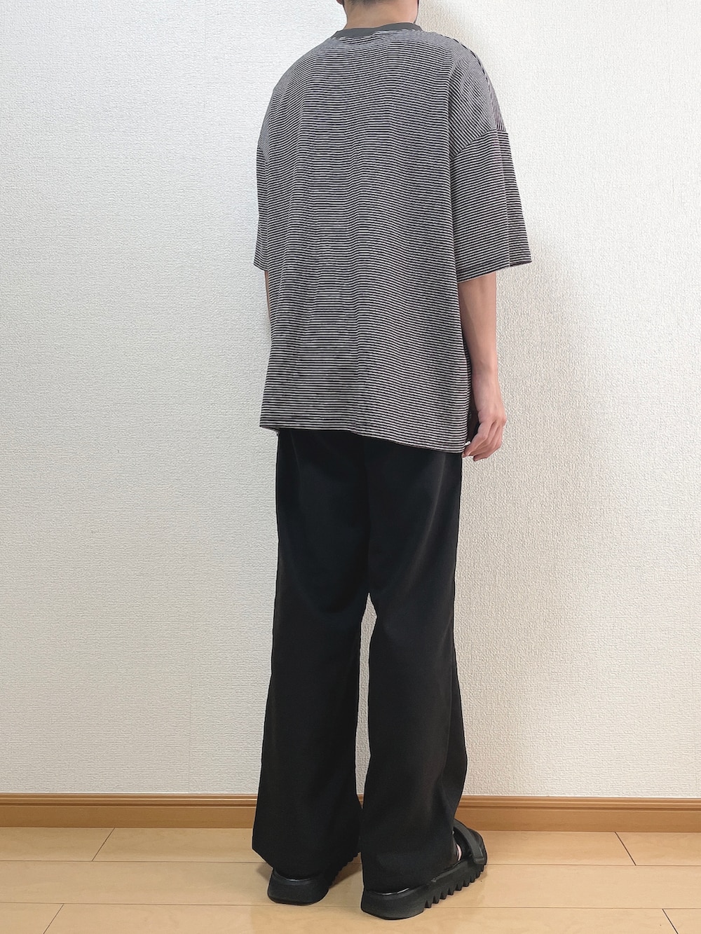 グレー系のTシャツ/カットソー、ブラック系のスラックス、ブラック系のサンダルを着用したメンズの秋コーディネートの4枚目の写真