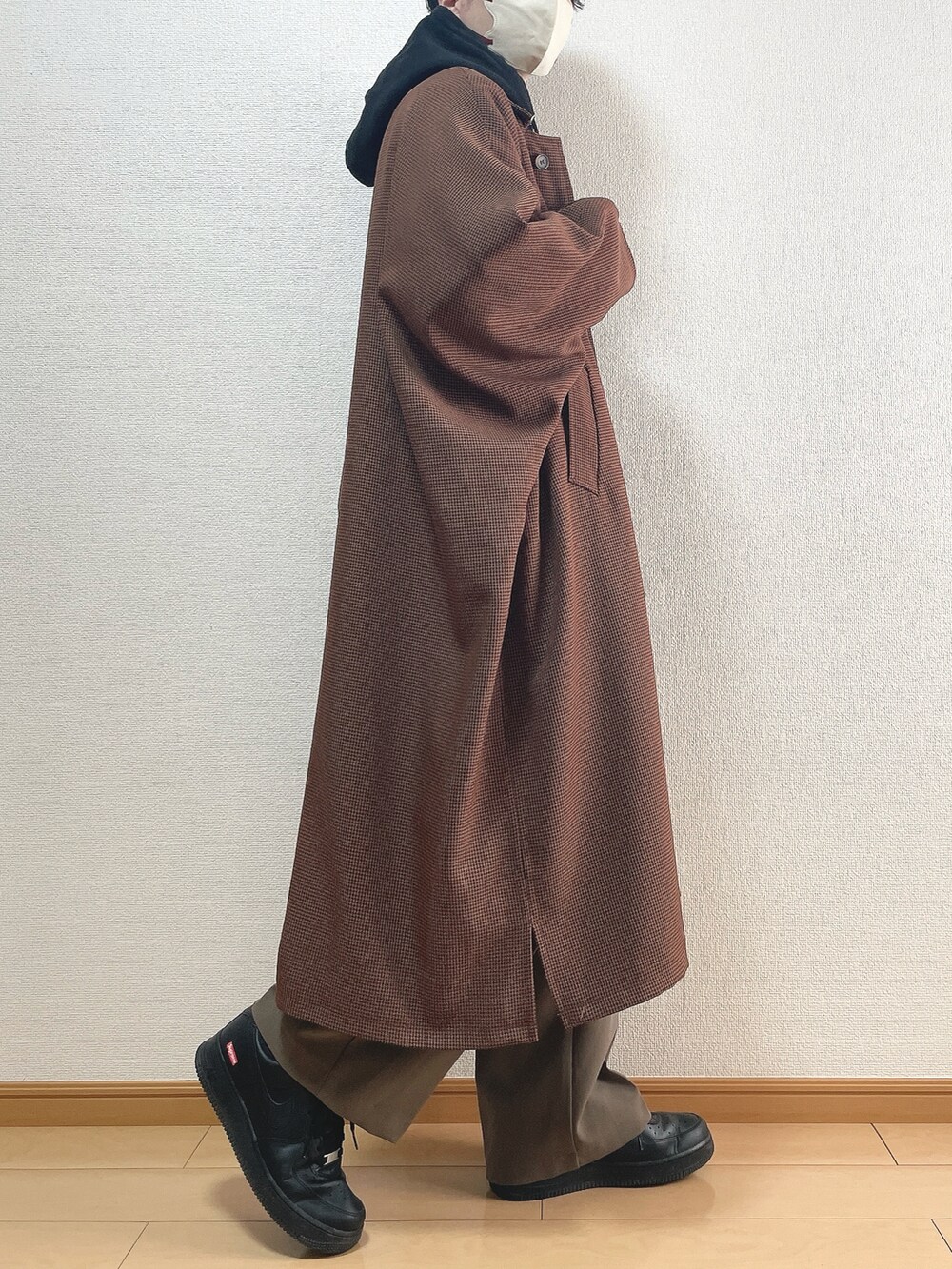 ブラウン系のステンカラーコート、ブラック系のパーカー、ブラウン系のその他パンツを着用したメンズの春コーディネートの2枚目の写真