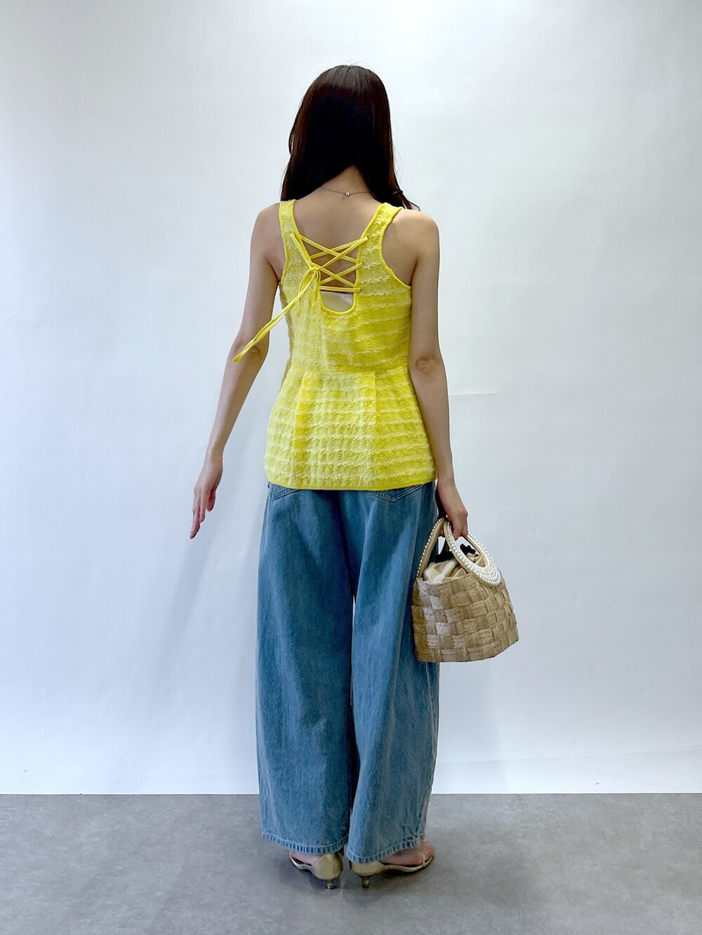 イエロー系のベスト、ベージュ系のトートバッグ、ブルー系のデニムパンツを着用したレディースの春コーディネートの3枚目の写真