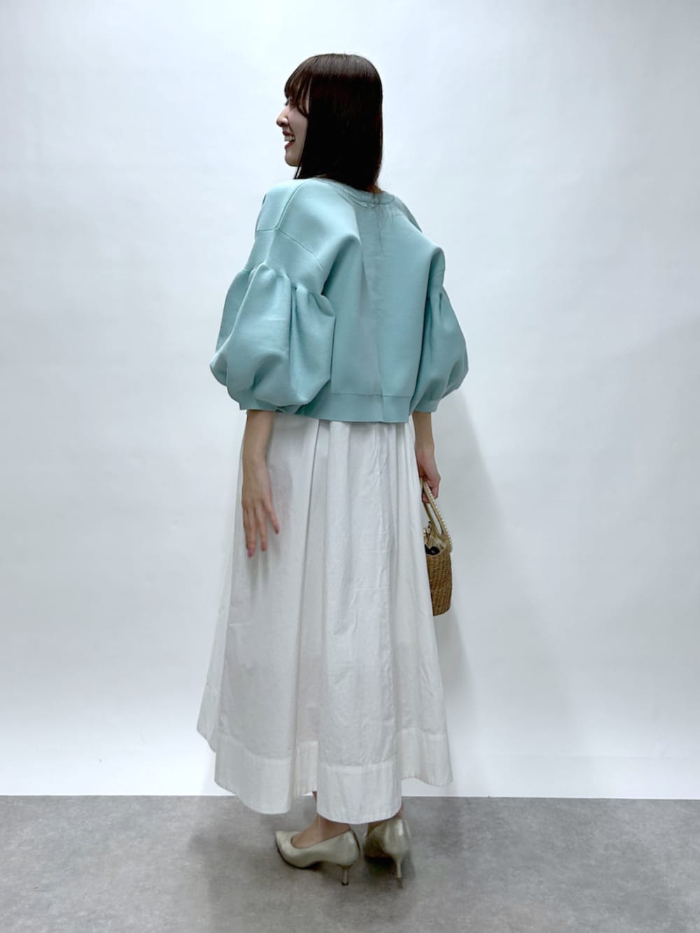 ベージュ系のかごバッグ、ホワイト系のワンピース、ブルー系のカーディガン/ボレロを着用したレディースの春コーディネートの3枚目の写真