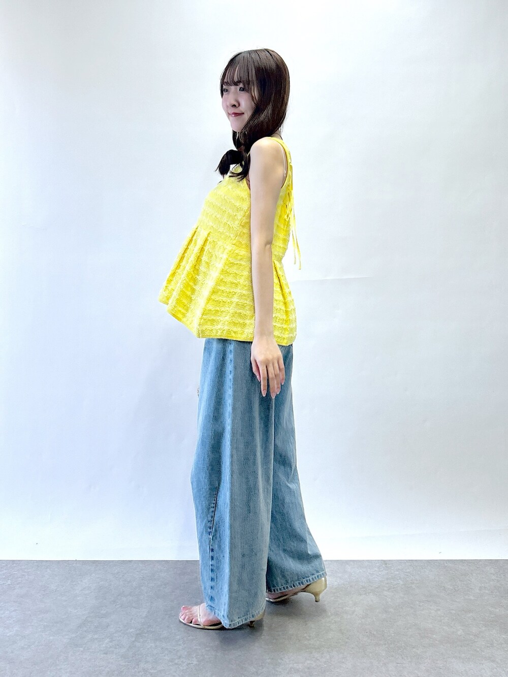 イエロー系のベスト、ベージュ系のトートバッグ、ブルー系のデニムパンツを着用したレディースの春コーディネートの2枚目の写真